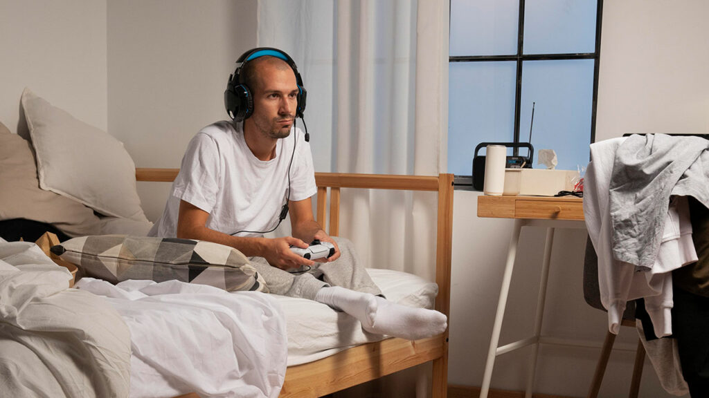 gamer sitting on bed with laundry mess